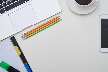 Top view of white desk with phone, stationery and a cup of coffe