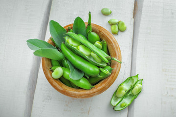 Bowl of podded green broad beans on a wooden table. Healthy organic food. Top view.
