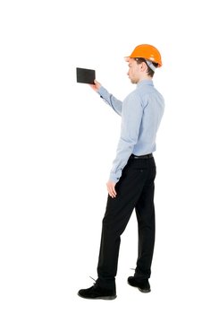 Backview of business man in construction helmet stands and enjoys tablet or using a mobile phone. Isolated over white. Curly businessman in a light jacket and a helmet shoots video on the tablet.