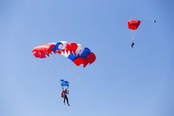 Papier Peint photo Sports aériens One skydiver on blue red white parachute, second skydiver on red parachute in clear blue sky