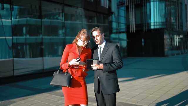 Young businessman make an offer with tablet PC to brown hair sexy attractive businesswoman in red dress. Handshake. Glossy district bg wide shot. Sunny day