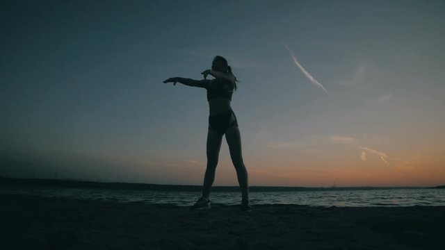 Young girl with a slender figure is engaged in gymnastics at sea at sunrise. Unrecognizable silhouette. HD.
