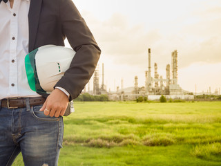 refinery engineer with white safety helmet see drawing standing in front of oil refinery building...