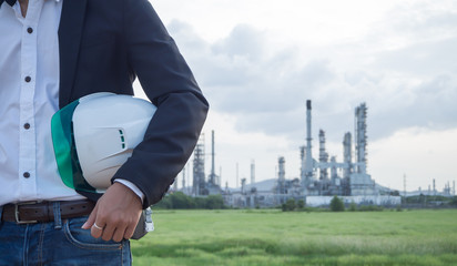 refinery engineer with white safety helmet see drawing standing in front of oil refinery building...