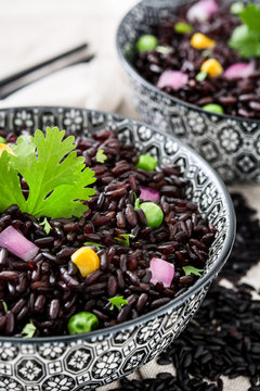 Black rice in a bowl and vegetables on white wooden table

