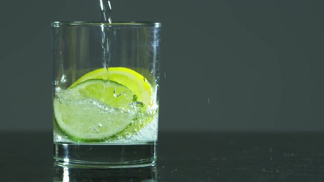 Water filling up a glass with a slice of lime and lemon