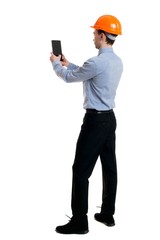 Backview of business man in construction helmet stands and enjoys tablet or using a mobile phone. Curly businessman in a light jacket and a helmet makes selfie tablet.