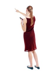 back view of pointing young beautiful girl with tablet computer. Isolated over white background. girl in the maroon sleeveless dress keeps your phone and shows a finger forward.