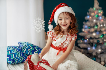 Beautiful red-haired little girl in a Christmas hat. The concept of the New Year and Merry Christmas