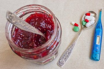 Various pills, spoon and thermometer. Raspberry jam.