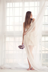 Young woman envelopes herself in the curtain while standing befo