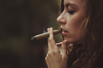 Profile of young woman with freckles on her cheeks smoking cigar