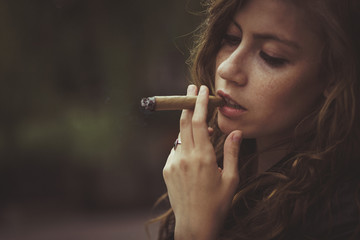 Lady holds cigar before her sensitive lips while standing though