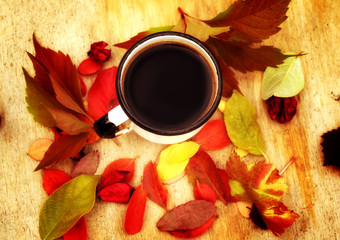 enamel coffee cup on the old wooden background in grunge style with autumn leaves rural retro style