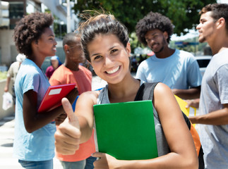 Laughing caucasian female student showing thumb with group of friends