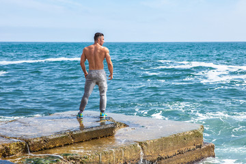 Man Athlete stands on a rock by the sea
