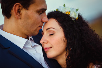 Daydreaming groom touches bride's forehead tender while she lean