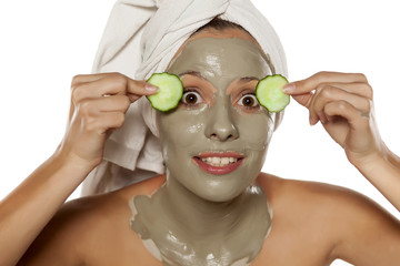 Young beautiful women posing with towel on her head, a mud mask on her face and cucumber slices