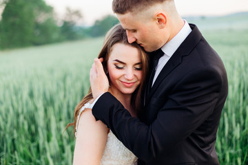 Nice bride enjoys groom's touch while they pose on the green fie