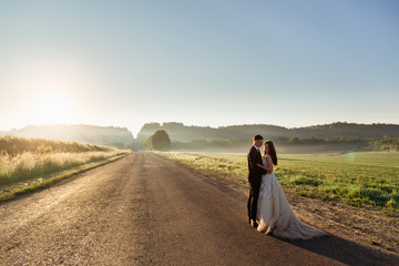 Evening sunlight illuminates pretty wedding couple standing on t
