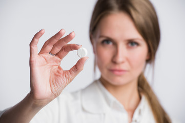 Serious medical woman with pill. Young beautiful nurse holding medicament on white.