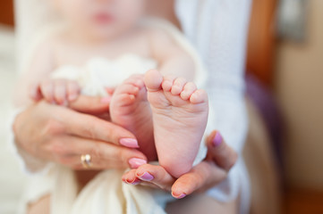 Mother holding little baby's feet on bed