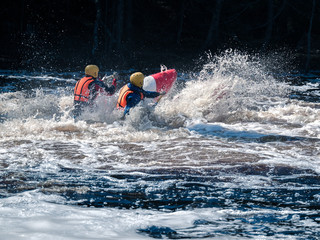 Toned image coordinated team of rowers in helmets and life jackets which sit on the raft, and...