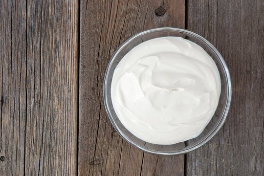 Greek yogurt in a clear bowl, above view on a rustic wood background