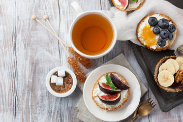 Bagels with different toppings - with cream cheese, figs, bananas, chocolate, blueberries for breakfast and a cup of tea on a rustic wooden table, top view