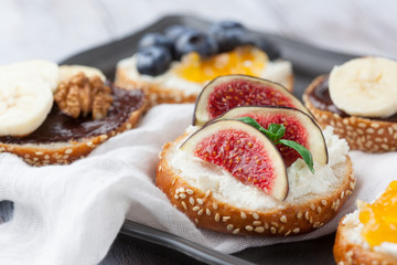 Bagels with different toppings - with cream cheese, figs, bananas, chocolate and blueberries for breakfast on a tray, selective focus