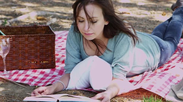Young woman reading and relaxing with a picnic in a park