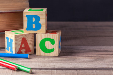 Wooden children's blocks with letters and colored pencils close-up, lie on a wooden table