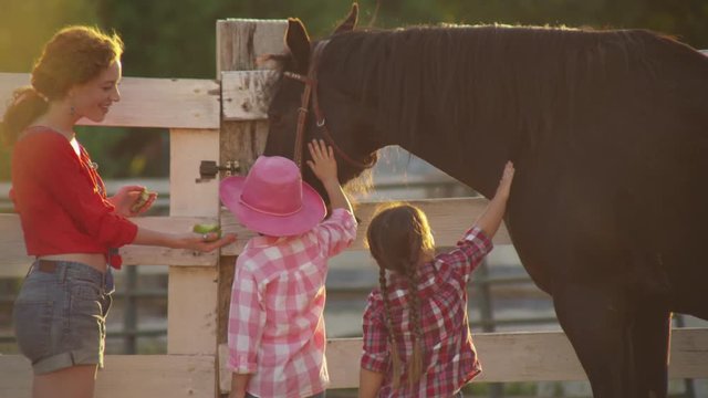 Mom with two young daughters feed apples to horses