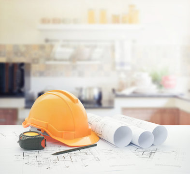 architectural blueprint with safety helmet and tools over modern kitchen interior as background