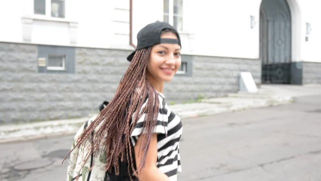 Young woman with dreadlocks put on the cap and walk by street