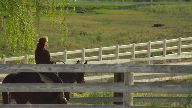 Blur in to young woman riding horse through ranch farm