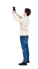 Back view of man with tablet. Standing young guy. Rear view people collection.  backside view of person.  Isolated over white background. Curly boy in a white warm sweater tablet takes something in