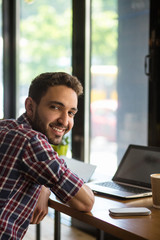 Portrait of happy handsome man working on laptop computer in restaurant or cafe. Cheerful man smiling for camera.