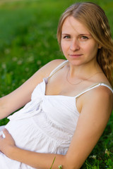 Naklejka na ściany i meble portrait of a pregnant woman sitting on the grass
