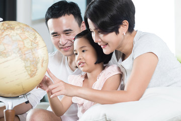 Asian parents exploring the globe with their child.