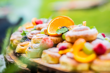 Catering buffet food outdoor. Cakes colorful fresh fruits berries oranges grapes and herb decorations.