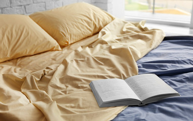 Fototapeta na wymiar Opened book on crumpled bed in room