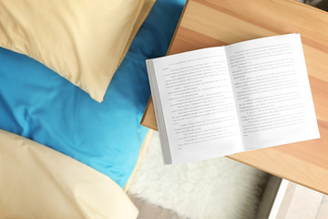 Fototapeta premium Opened book on wooden bedside table near crumpled bed