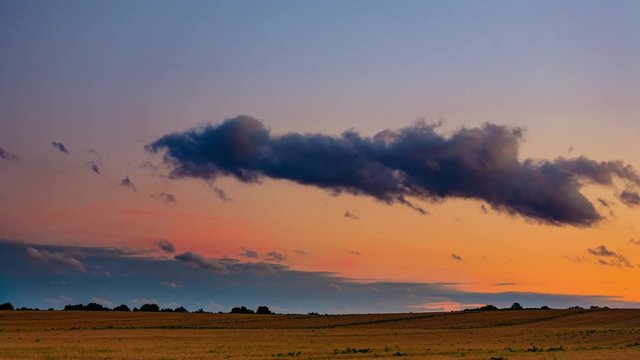 Colorful sunset over wheat field with moving clouds time lapse.