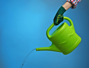Hand in glove pouring water from watering can on color background