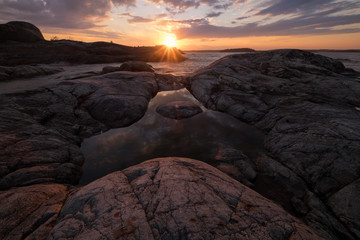 The rays of the setting sun glows the cracks in the granite rocks that surround a small pond in shape of triangle on the island Taakionluodot, Russia, Karelia