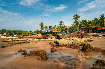 Fototapeta na wymiar Guesthouses and sunbeds on the shore of the Arabian Sea in the middle of rocks and sandstone in Ashvem, Goa, India