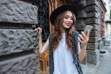 Young smiling beautiful brunette girl listens music with earphones outdoors