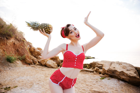 Smiling beautiful pinup girl in headband posing with pineapple