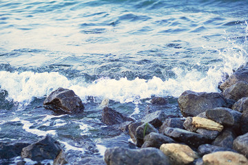 Strong sea wave splashing on the rocky shores; selective focus; toned image